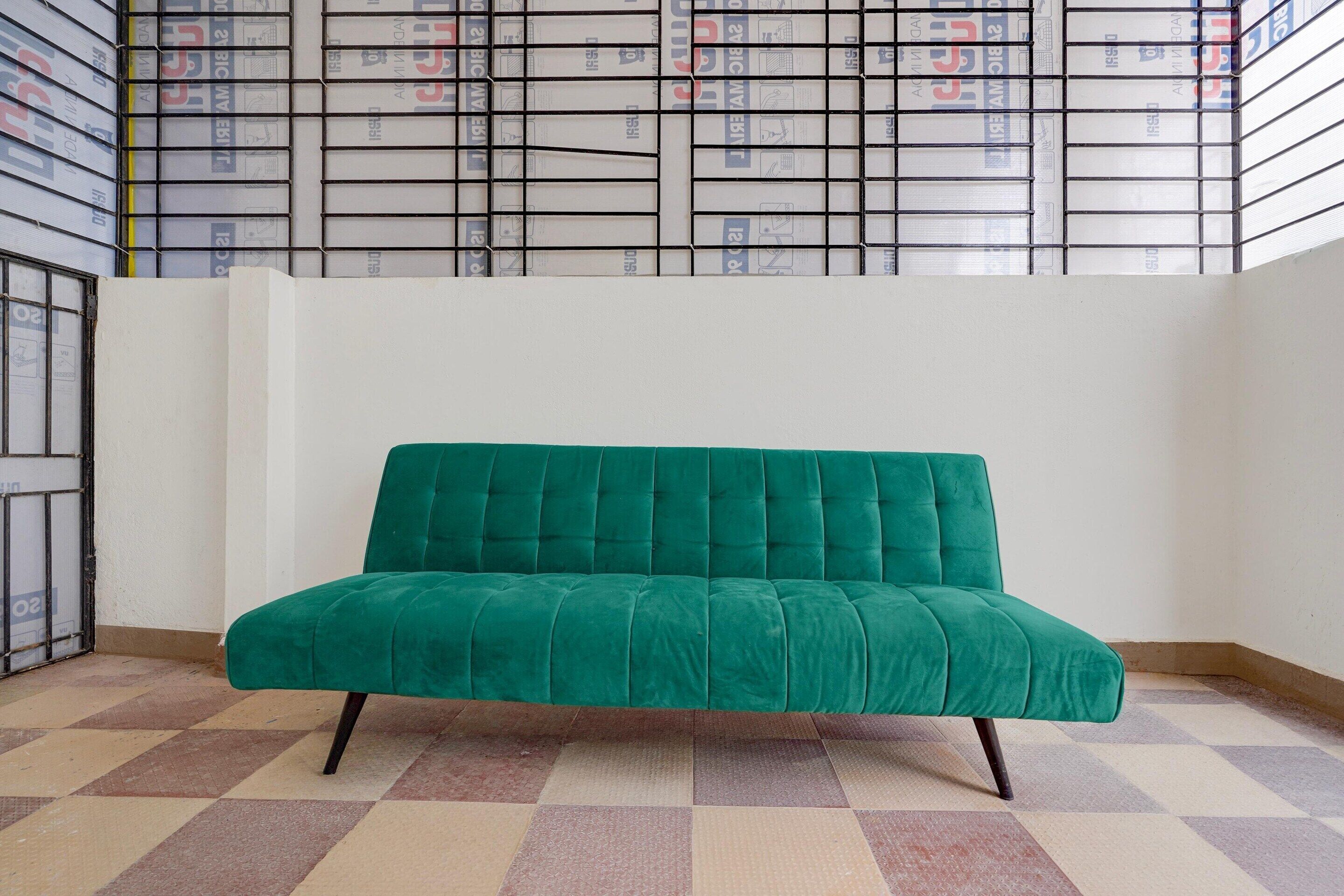 A green sofa in a room with a patterned floor and a white wall.