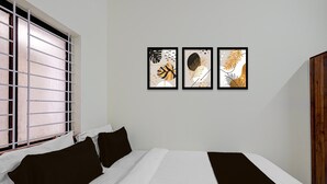 Ein Hotelzimmer mit einem Bett, einem Fenster mit Jalousien und drei gerahmten Kunstwerken an der Wand.