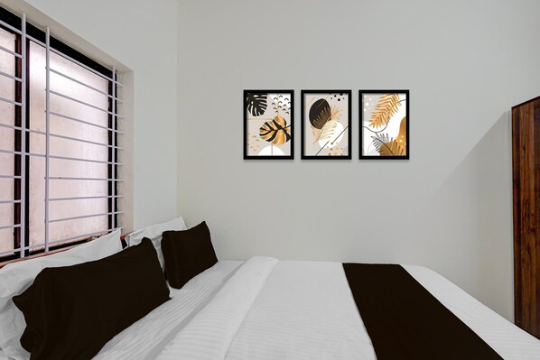 A hotel room with a bed, a window with blinds, and three framed artworks on the wall. - Classic Seven Hills (Bengaluru)