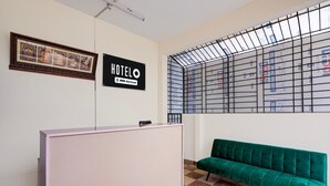 Ein Empfangsbereich mit einer Rezeption, einem grünen Sofa, einem gerahmten Bild und einem Schild, das anzeigt, dass das Hotel von OYO bewirtschaftet wird.