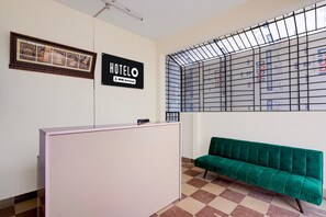 Ein Empfangsbereich mit einer Rezeption, einem grünen Sofa, einem gerahmten Bild und einem Schild, das anzeigt, dass das Hotel von OYO bewirtschaftet wird.