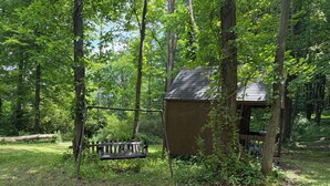 A wooden deck with a swing, surrounded by trees and a small shed.
