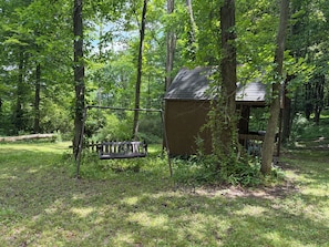 A wooden deck with a swing, surrounded by trees and a small shed.