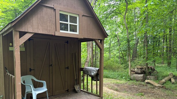 A wooden cabin with a porch, a plastic chair, and a small table.