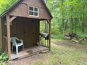 A wooden cabin with a porch, a plastic chair, and a small table.
