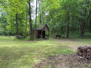 A small wooden cabin with a porch, surrounded by a forested area.