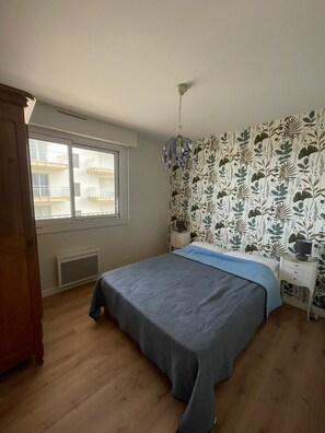Un dormitorio con cama, ventana, radiador, armario de madera y pared con motivo de hojas.