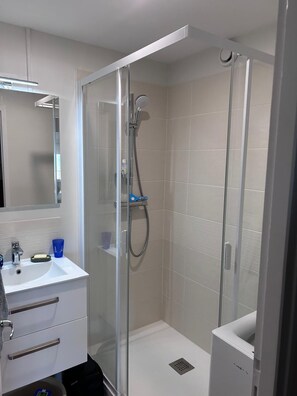 Un baño moderno con ducha de vidrio, un lavamanos blanco con espejo y un armario de almacenamiento.