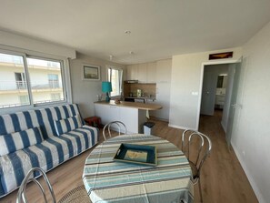 Un espacio habitable compacto con sofá, mesa de comedor, kitchenette y vista al balcón.