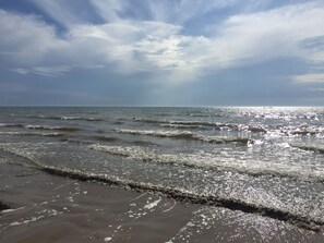 Uma praia com ondas, céu claro e horizonte distante.