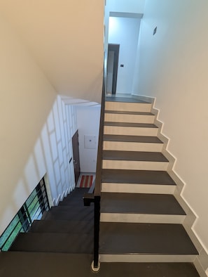 Una escalera con barandilla que conduce a un rellano con una puerta y un interruptor de luz.