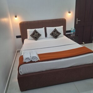 Una cama bien hecha con dos almohadas, un cabecero marrón y un par de toallas enrolladas en el pie de la cama.