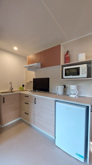 Cozinha compacta com micro-ondas, cafeteira e pequena geladeira.