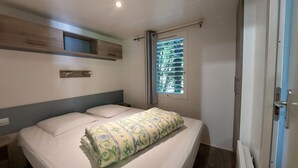 A bedroom with a bed, a window with blinds, a wooden shelf, and a door.