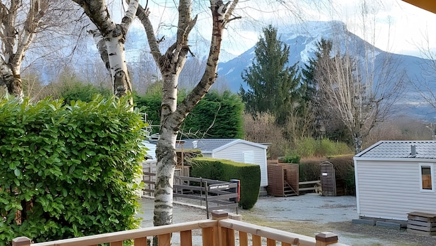 A cabin with a wooden deck, a small shed, and a well-maintained hedge.