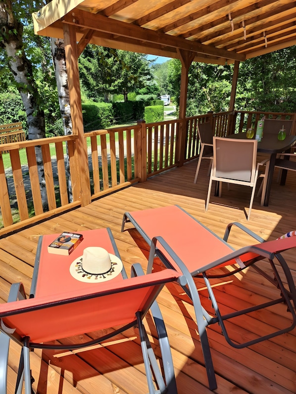 Een houten terras met een tafel, stoelen, een pergola en uitzicht op een groen landschap.