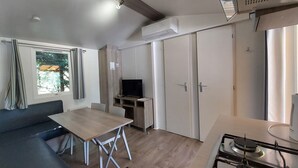 A compact living space with a sofa, dining table, TV, and kitchenette. - Confort 2 Mobile Home with Mountain View, Wi-Fi & Air Conditioning (Saint-Laurent-en-Beaumont)