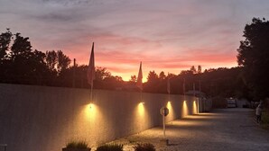 A sunset view with a paved area, potted plants, and a building in the background. - Confort 2 Mobile Home with Mountain View, Wi-Fi & Air Conditioning (Saint-Laurent-en-Beaumont)