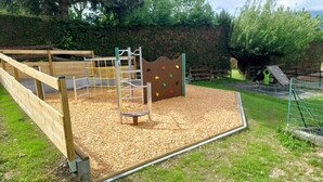 A playground with a wooden climbing structure, a slide, and a fenced area. - Confort 2 Mobile Home with Mountain View, Wi-Fi & Air Conditioning (Saint-Laurent-en-Beaumont)