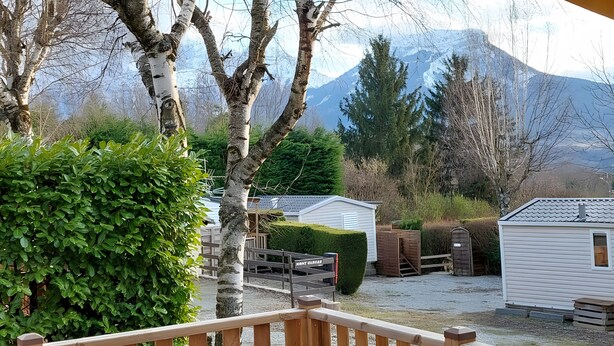 A cabin with a wooden deck, a small shed, and a well-maintained hedge. - Confort 2 Mobile Home with Mountain View, Wi-Fi & Air Conditioning (Saint-Laurent-en-Beaumont)