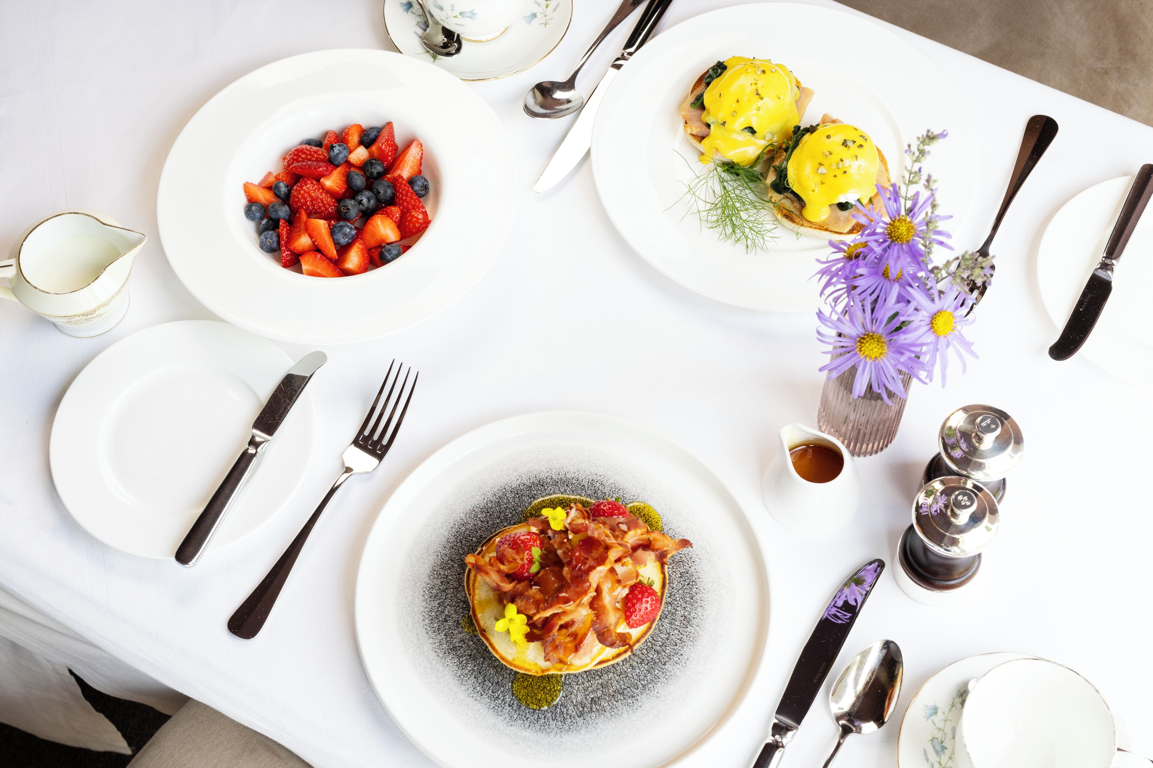 Una mesa dispuesta con platos de comida, cubiertos y un jarrón con flores.