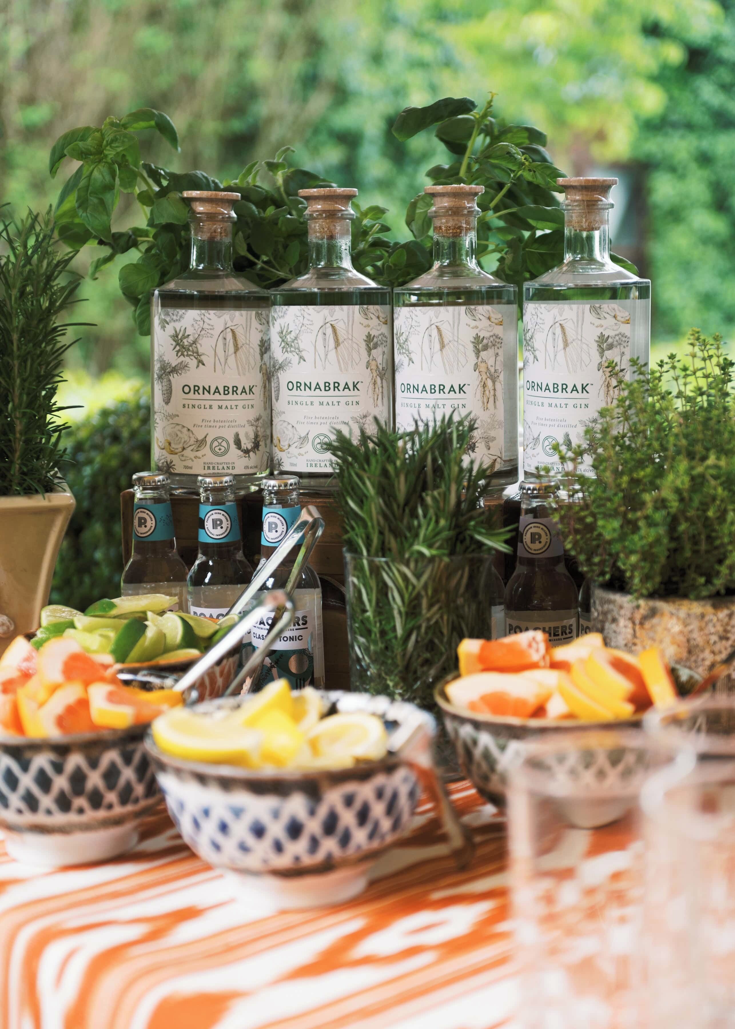 A table with bottles of Ornabrak gin, bowls of fruit, and a glass of tonic water.