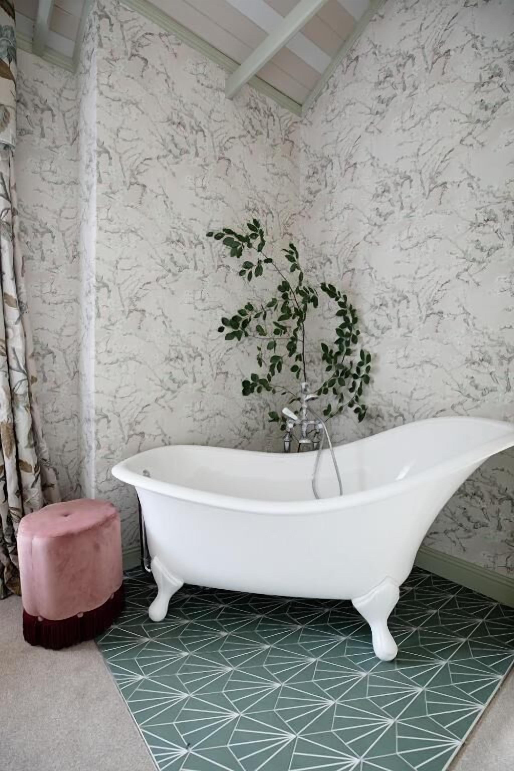Un baño con una bañera independiente, un taburete pequeño y una planta.