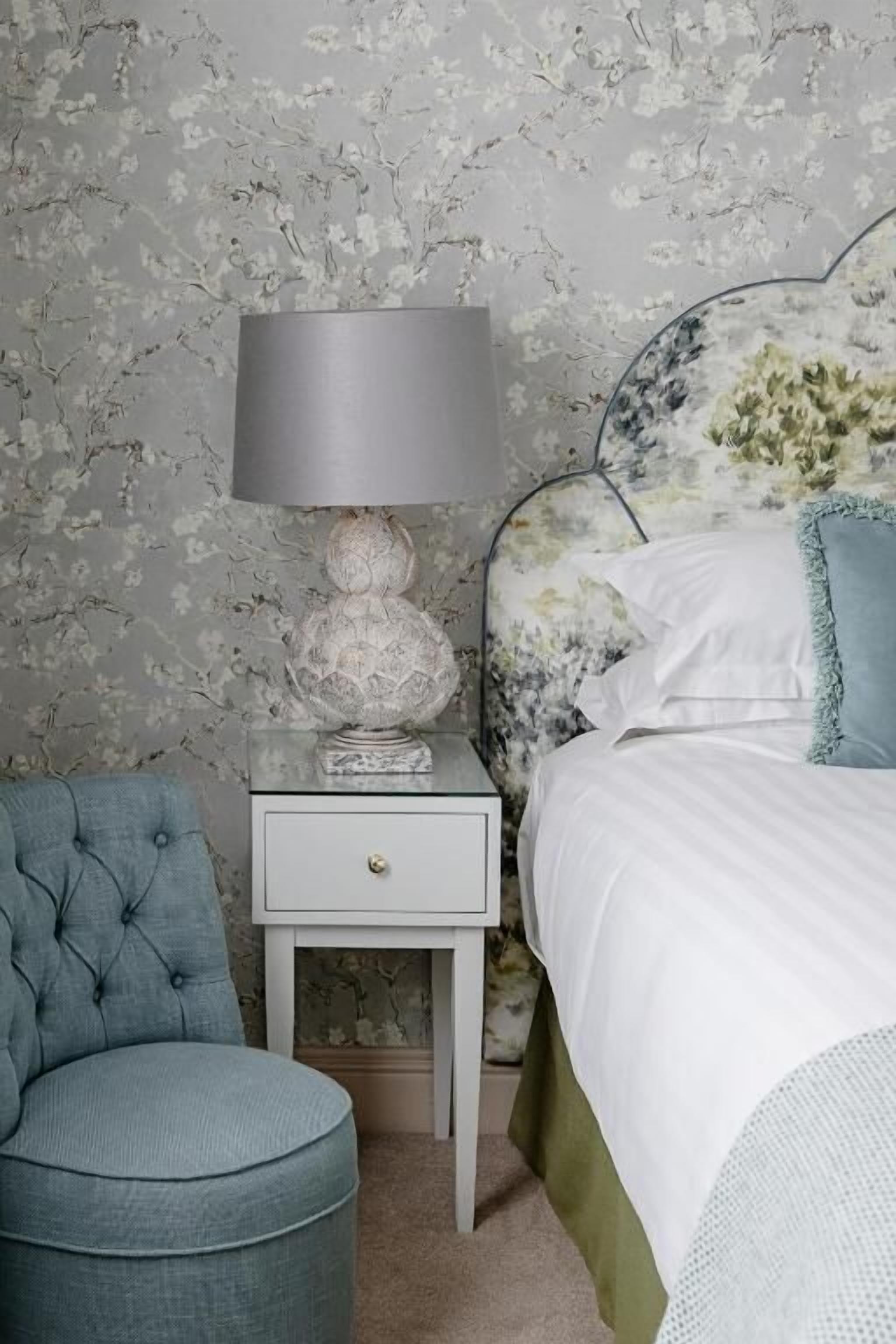 A bedroom with a bed, a nightstand with a lamp, a chair, and a dresser.