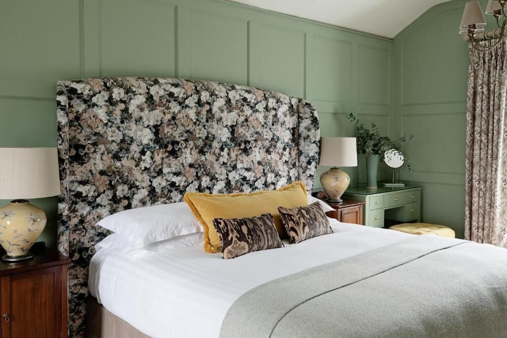 Una cama con cabecera de flores, ropa de cama blanca y almohadas decorativas.