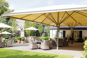 Eine Außenpatio-Terrasse mit Korbmöbeln, Sonnenschirmen und Kübelpflanzen.