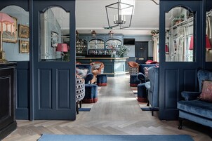 A room with a bar area, seating with ottomans, and a herringbone wood floor.