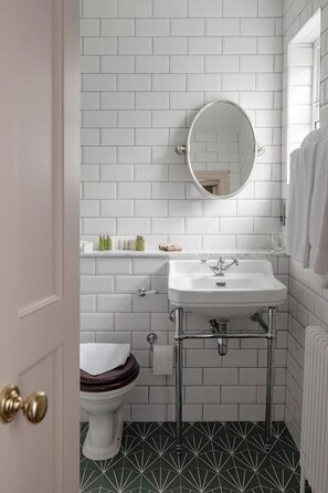 A bathroom with white subway tiles, a white sink, a round mirror, a toilet, and a patterned floor. - The Station House Hotel  (Kilmessan)