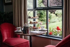Un juego de servicio para té de tres niveles sobre una mesa junto a una ventana con vistas a un jardín.
