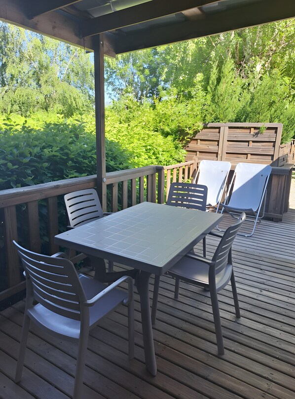 Eine überdachte Terrasse im Freien mit Tisch und Stühlen, umgeben von üppiger Vegetation.