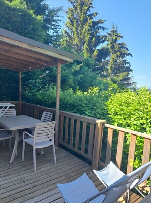 Eine Holzterrasse mit Tisch und Stühlen, umgeben von üppiger Vegetation und hohen Bäumen.