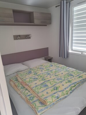 Ein Schlafzimmer mit Bett, Nachttisch, eingebautem Regal und Fenster mit Jalousien.