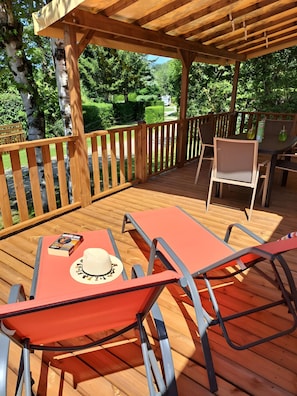 En träaltan med ett bord och stolar, en pergola och utsikt över ett grönskande landskap.