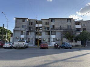 Un edificio de varios pisos con fachada plana, coches aparcados y motocicletas en la entrada.