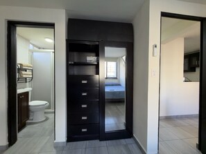 Una habitación con armario, cama y baño visible a través de una puerta abierta.