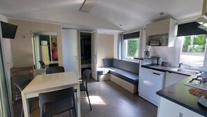 A compact kitchen with a dining area, a built-in bench, a microwave, a sink, and a window with a view. - Premium 2 Mobile Home with Mountain View, Wi-Fi, and Air Conditioning (Saint-Laurent-en-Beaumont)