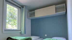 A room with two beds, a window with curtains, a ceiling light, and a built-in shelf above the beds. - Premium 2 Mobile Home with Mountain View, Wi-Fi, and Air Conditioning (Saint-Laurent-en-Beaumont)