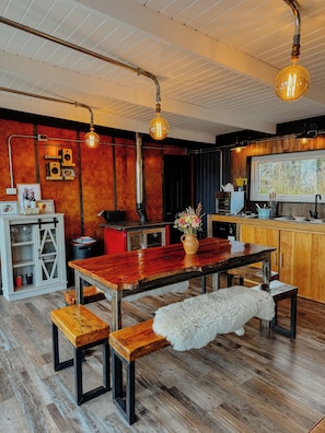 A modern kitchen with wooden cabinets, a large window, and a dining area with a wooden table and benches.