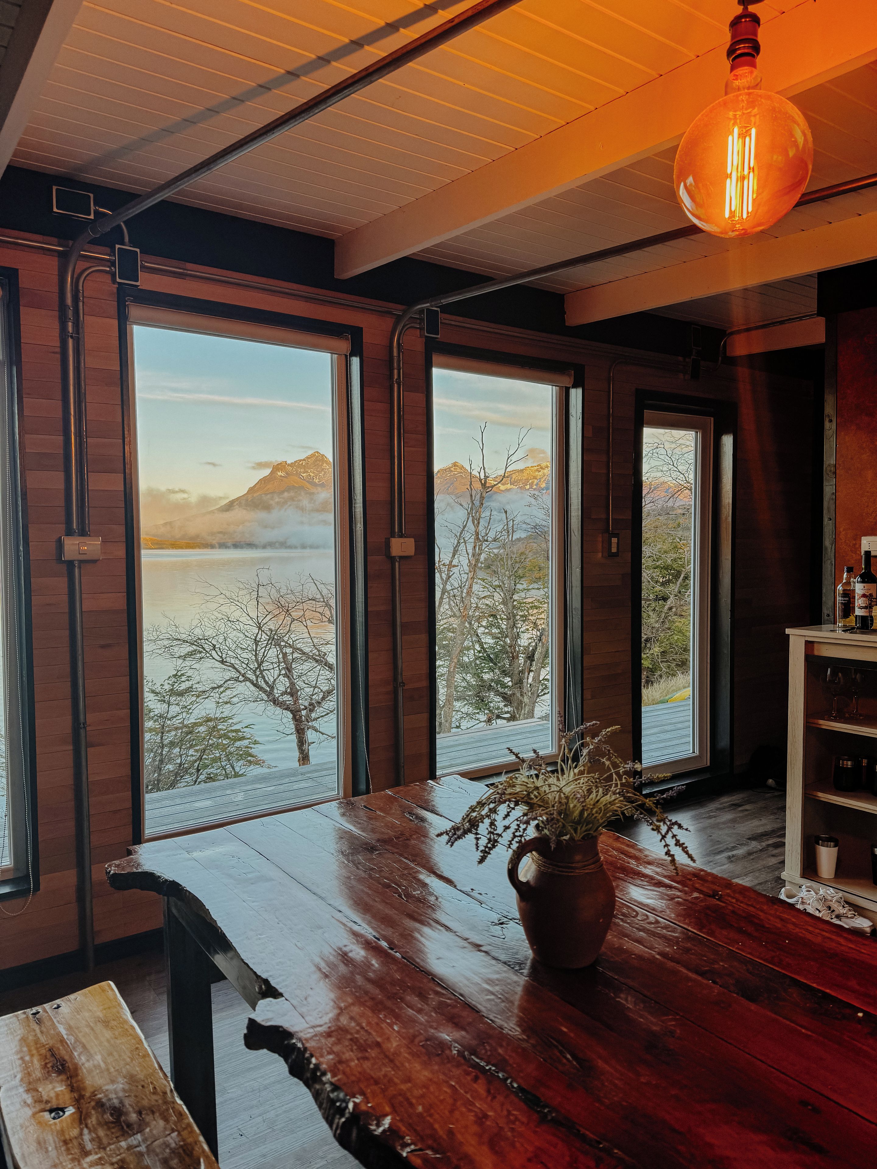 A room with large windows, a wooden table, and a hanging light fixture.