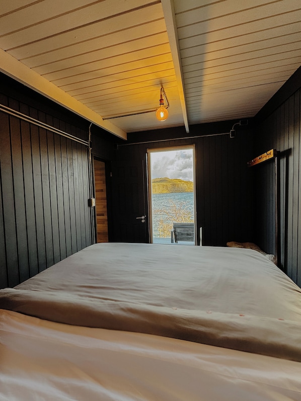 A bedroom with a large bed, a view of a landscape through an open door, and a hanging light fixture.