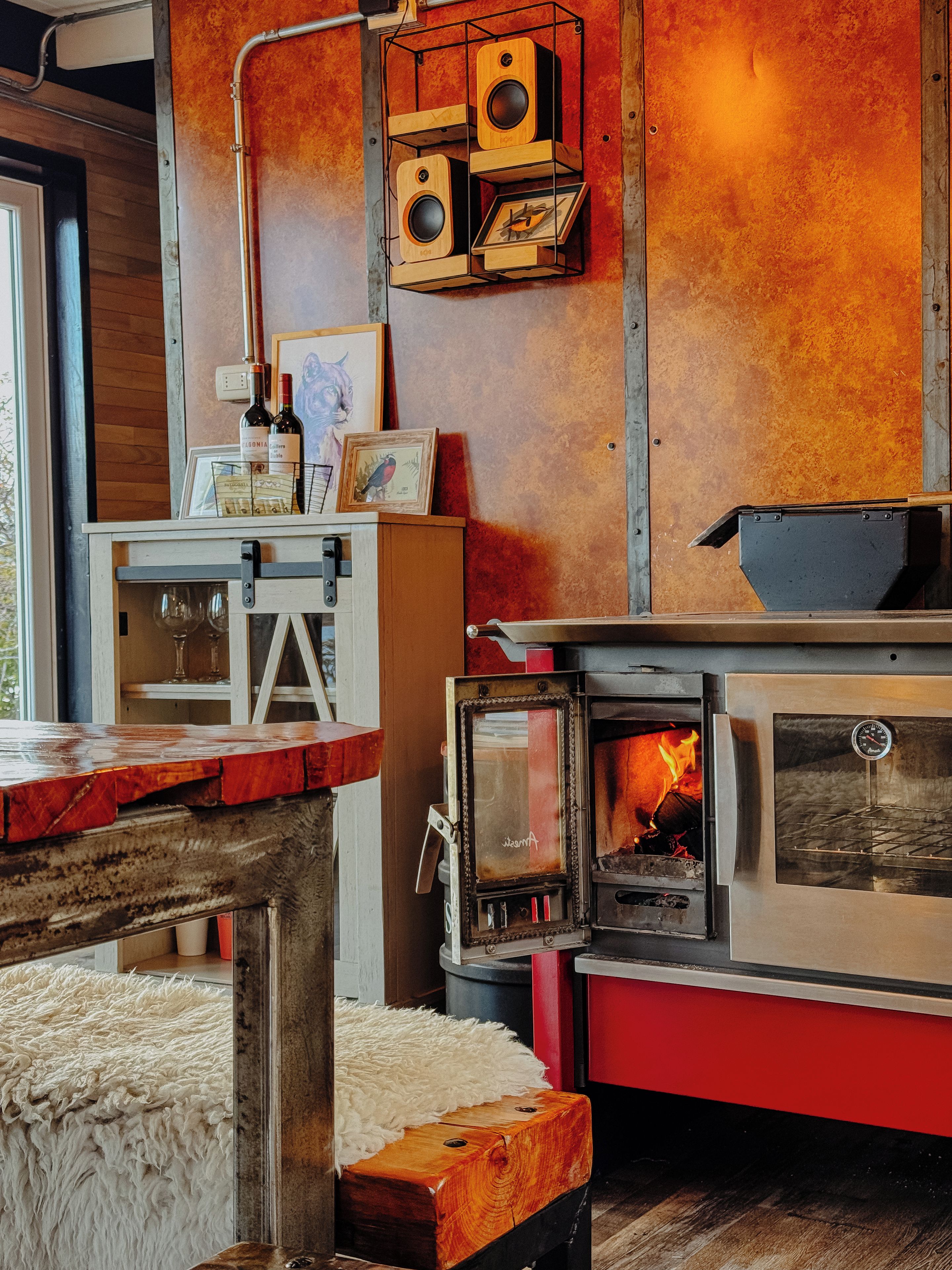 A rustic interior with a wood-burning stove, a wooden shelf with speakers, and a framed picture on a table.