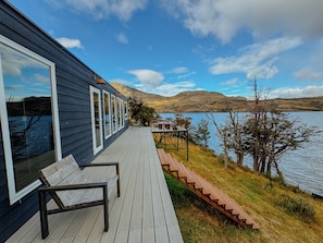 A deck with a wooden bench, overlooking a lake with mountains in the background.