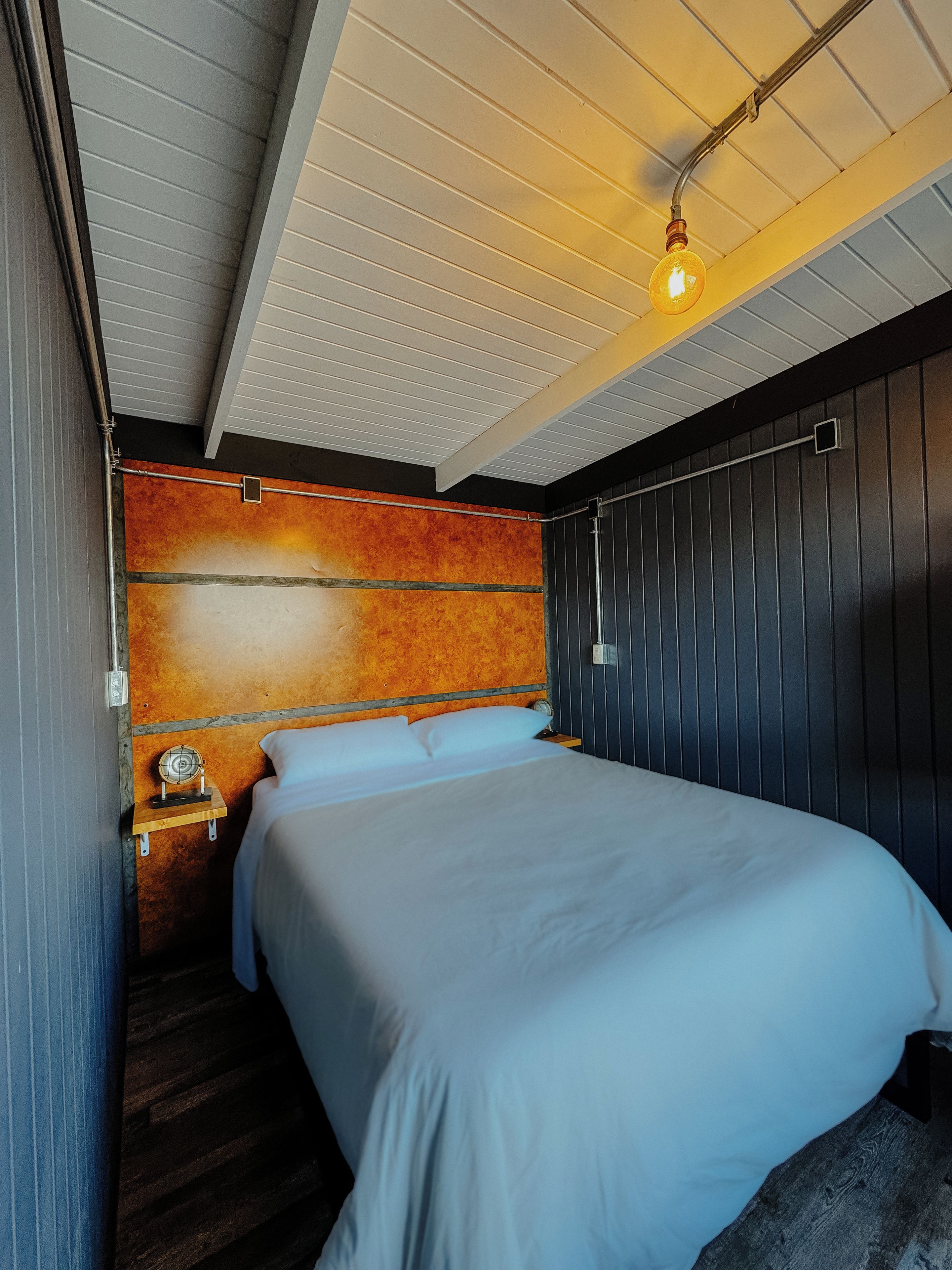 A hotel room with a bed, a nightstand, a wall-mounted heater, and a ceiling light fixture.