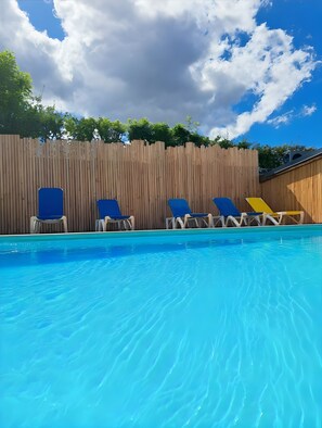 Piscina com espreguiçadeiras azuis e um cercado de madeira ao fundo.