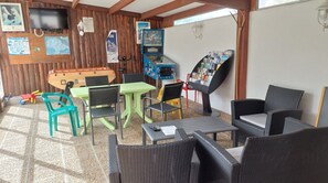 Een kamer met een tafelvoetbaltafel, een groene tafel, rieten stoelen, een boekenkast, een televisietoestel en een kaart aan de muur.