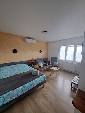 A room with a bed, two chairs, a small table, and a window with blinds.